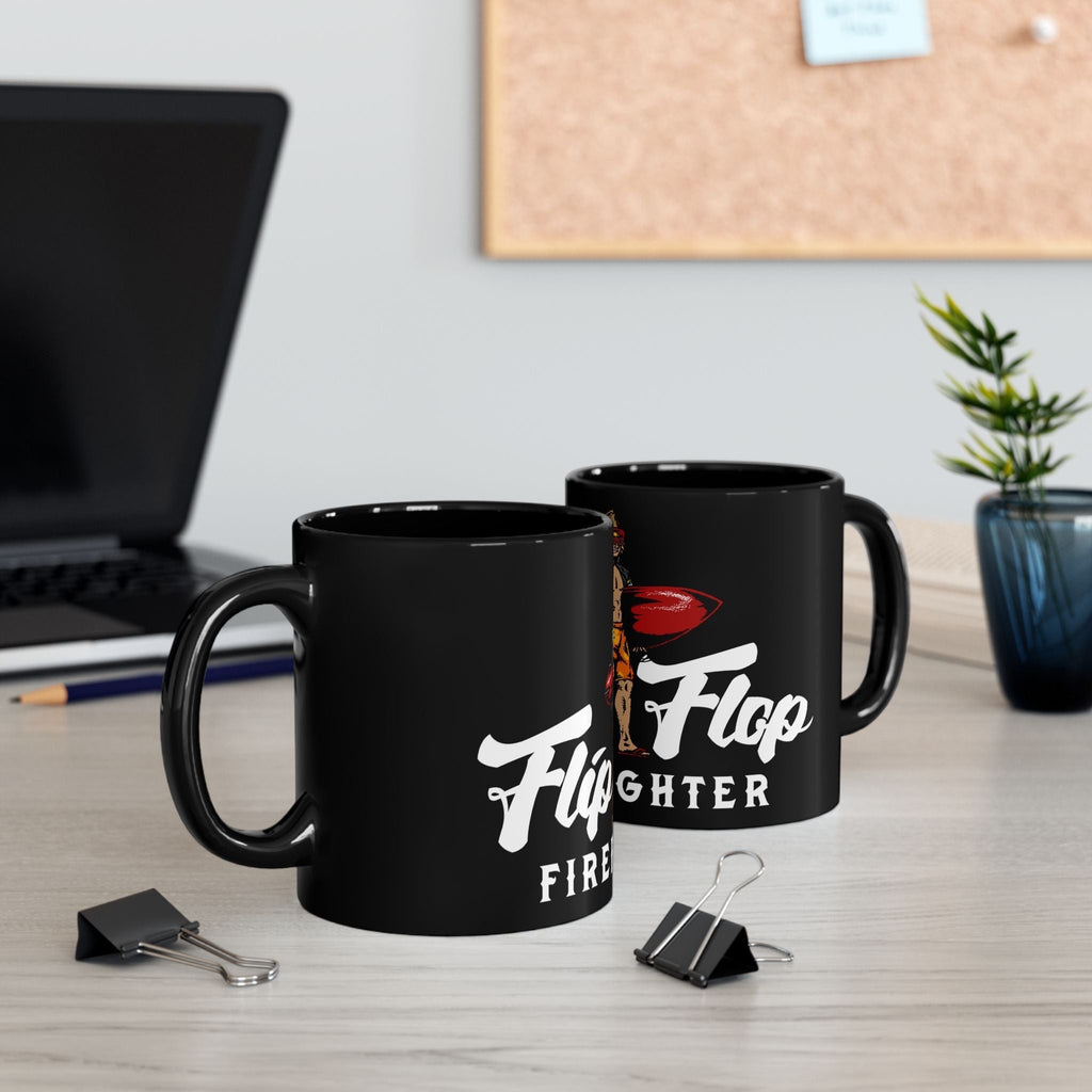 Flip Flop Firefighter glossy black ceramic coffee mug with surfer graphic on a desk with a laptop and plant.