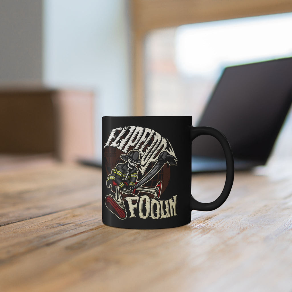 Flip Flop Firefighter glossy black ceramic coffee mug with a skeleton firefighter graphic on a wooden desk.