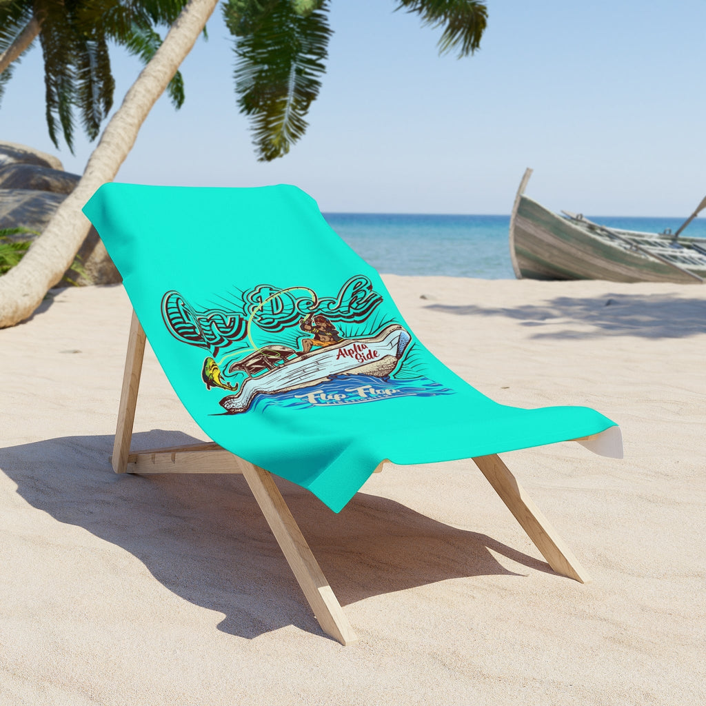 Flip Flop Firefighter turquoise beach towel with boat artwork draped over a wooden chair on a sunny sandy beach.