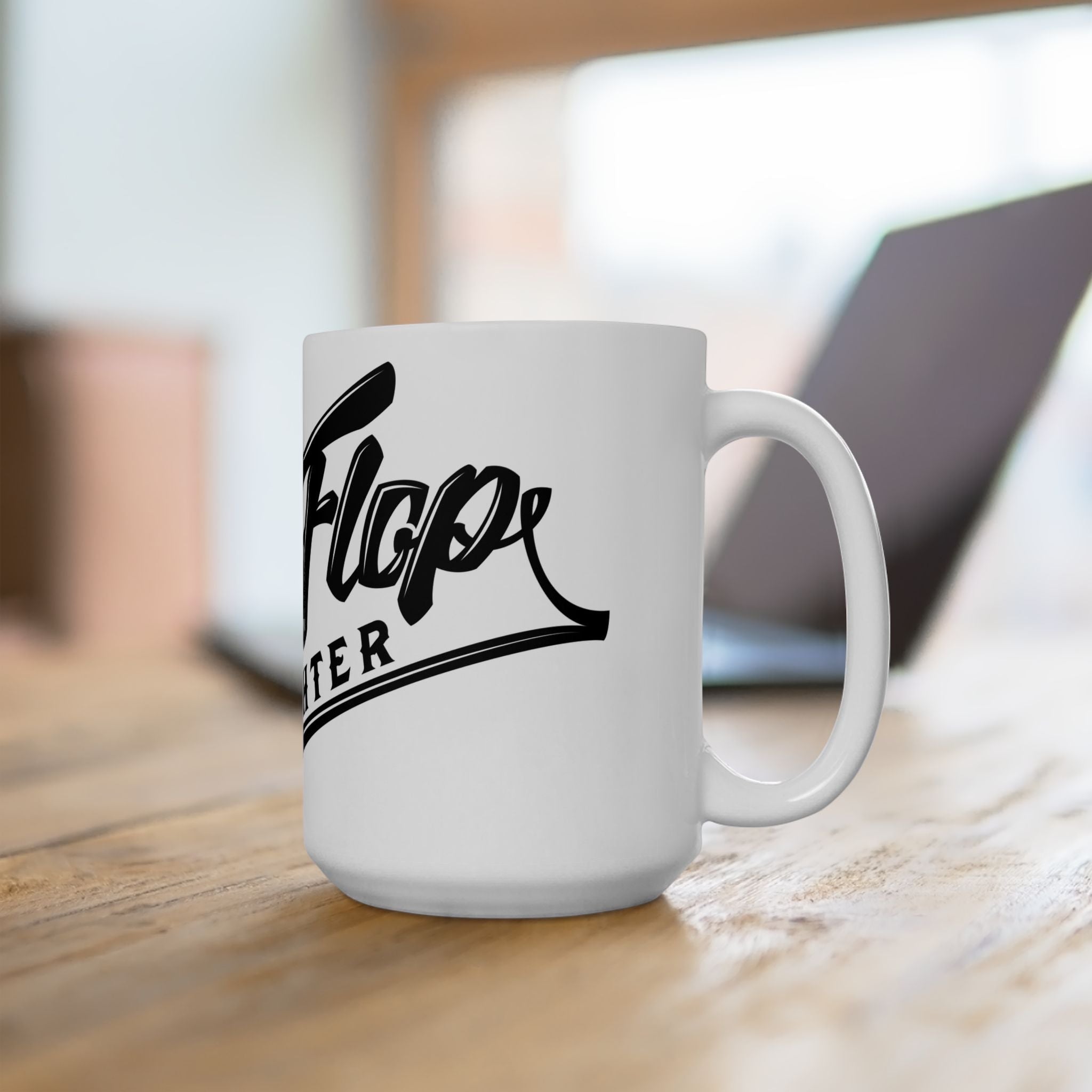 Flip Flop Firefighter white ceramic coffee mug with black logo on a wooden desk with a laptop in the background.