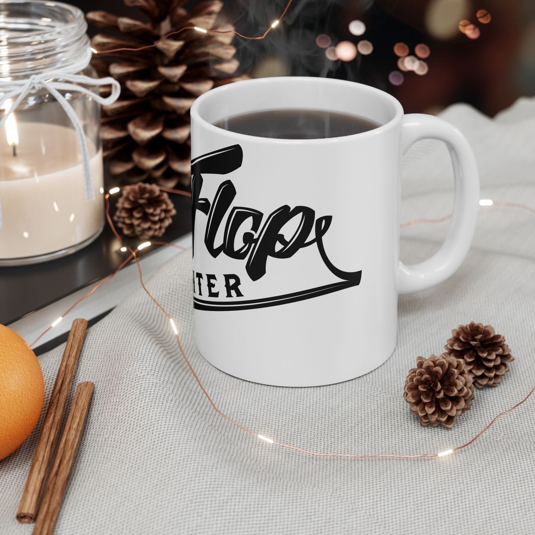 Flip Flop Firefighter white ceramic coffee mug with black logo, styled on a table with pinecones and fairy lights.